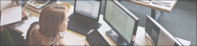 Osoba siedzi przy biurku z laptopem i komputerem